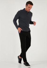 Cămașă polo cu mâneci lungi de culoare gri închis, cu o textură ribitată și guler, combinată cu pantaloni negri slim-fit și adidași negri.