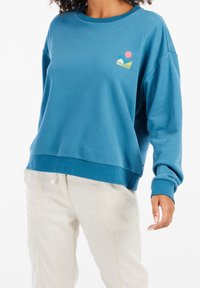 Felpa blu dal taglio comodo, con polsini e orlo a coste. Presenta un logo multicolore sul petto. Tessuto morbido con una texture liscia.