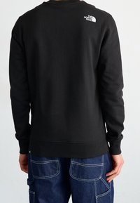 Sudadera negra con cuello y puños acanalados; presenta un pequeño logo blanco en la parte superior de la espalda. Combinada con pantalones cargo azul oscuro.