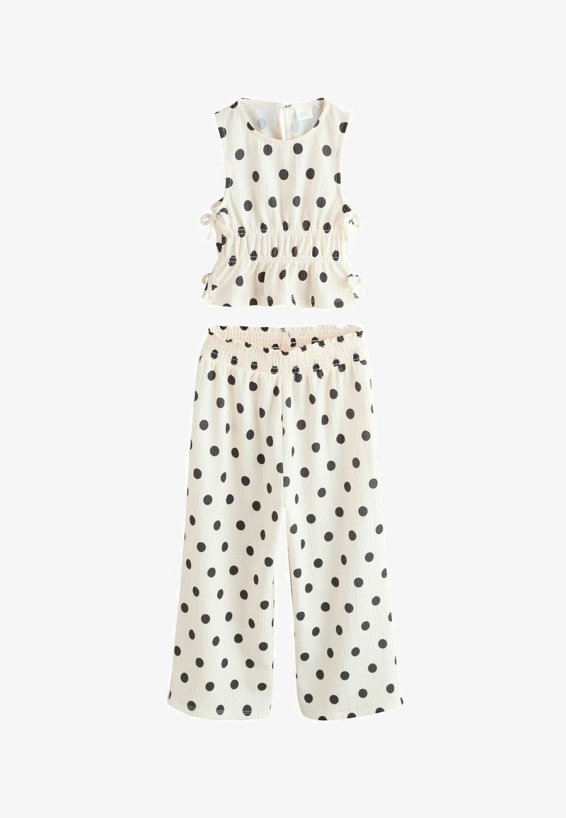 Komplet brezrokavnika belega topa in širokih hlač s črnimi pikami, ki ima na vrhu stranske trakove in elastični pas na hlačah.