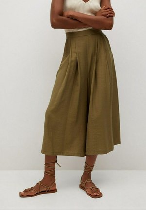 Oliwkowe, szerokie kuloty z plisowanym przodem, wykonane z lekkiego materiału, zestawione z brązowymi płaskimi sandałami z krzyżującymi się paskami.