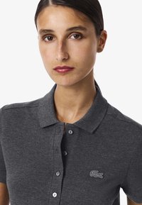 Mörkgrå pikétröja i texturerat tyg, med klassisk krage, knappslå och broderad logotyp på bröstet.