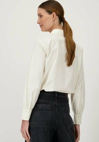 Lichtgekleurde, langemouw blouse met hoge kraag en knoopmanchetten, gecombineerd met zwarte, hoge taille jeans. Glad stoftextuur.