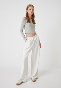 Helles graues, kurzes Langarmtop mit schulterfreiem Design, kombiniert mit lockeren, weißen Sweatpants. Beide Teile bieten eine weiche Textur und einen lässigen Stil.