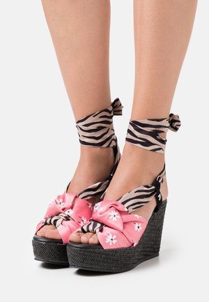 Sandales compensées avec une semelle noire tissée, un nœud en tissu à motif floral rose et des liens à imprimé zèbre à la cheville. Design ouvert qui révèle les orteils.