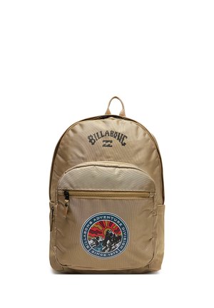 Tan Billabong rygsæk med frontlomme og en rund badge, der viser en surfer, sol og bølger med teksten "Adventure Division since 1973."