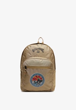 Tan Billabong rygsæk med frontlomme og en rund badge, der viser en surfer, sol og bølger med teksten "Adventure Division since 1973."