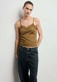 Rjav top z zapeljivim čipkastim robom, povezan z temno denim jeans hlačami. Top ima tanke naramnice in prilegajoč silhueto.