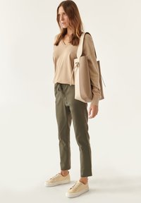 Suéter de pico beige, pantalones verde oliva con botones en la parte delantera y zapatillas ligeras beige. El bolso es estructurado con un diseño elegante.