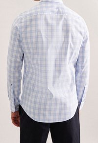Jasnoniebieska i biała koszula w kratę z długim rękawem, zaokrąglonym dołem, zapinanymi na guziki mankietami oraz miękką fakturą tkaniny. Posiada tylną karczek.