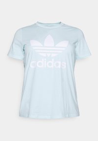 Ljusblå bomulls-T-shirt med en stor vit Adidas-logotyp och tre horisontella ränder under en blommig emblem. Korta ärmar, rund hals.