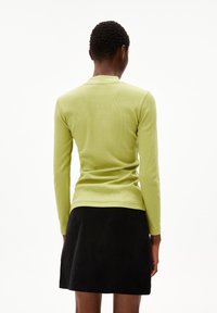 Langarm, ribbelshirt in levendig limoen groen, gecombineerd met een zwarte corduroy rok. Het shirt heeft een aansluitend ontwerp en een ronde halslijn.