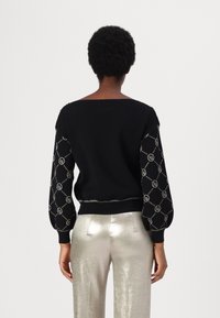 Pull noir avec des manches bouffantes brodées en argent. Comprend un col rond et un ourlet côtelé. Associé à un pantalon argenté métallique.