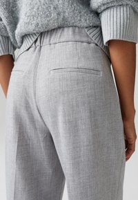 Grijze getextureerde broek met een ontspannen pasvorm, voorzien van een tailleband en achterzakken. De stof heeft een subtiel visgraatpatroon.