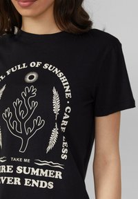 T-shirt en coton noir avec un design graphique blanc comprenant des motifs de corail et de feuilles. Le texte indique « Plein de soleil », « Prends-en moins soin », et « Emmène-moi ».