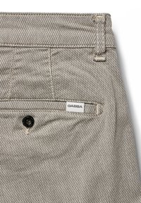 Svetlo sivi hlače s vzorcem iz teksturirane tkanine. Imajo oznako GABBA in črn gumb na pasu.