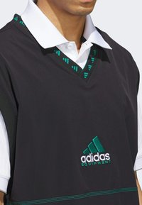 Gilet sans manches noir avec un col blanc, comportant des motifs géométriques teal et le logo "adidas EQUIPMENT" brodé en vert et blanc.