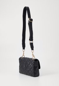 Černá prošívaná kabelka s texturovaným povrchem, detailem s logem a odnímatelným ramenním popruhem se zlatou kovovou výbavou.