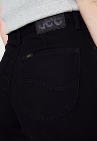 Black denim jeans featuring a single rear pocket with decorative stitching, a leather brand tag, and a smooth texture.