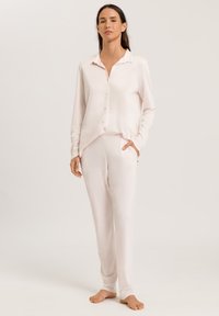 Lichtroze loungewear set bestaande uit een knoopsluiting met lange mouwen en een kraag, en bijpassende elastische taillebroek, gemaakt van een gladde stof.