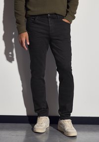 Jeans ajustados negros con una textura suave, que cuentan con cinco bolsillos, una cremallera en la bragueta y un sutil efecto de desgaste. Combinados con zapatillas de color claro.
