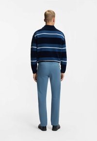 Námořnický pruhovaný fleecový svetr s světle modrými a bílými pruhy, spárovaný se světle modrými kalhotami a černými botami. Model je viděn zezadu.