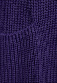 Close-up van paarse gebreide stof met verticale ribbelstructuur en verweven garenlussen die een zachte, rekbare oppervlakte creëren.