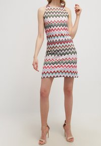 Robe sans manches en tricot avec un motif en zigzag rose, vert, bleu et rouge. Silhouette ajustée avec un col haut, s'arrêtant au milieu de la cuisse.