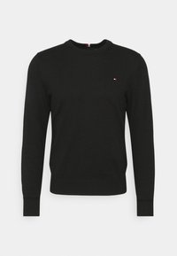 Pull en maille noire avec manches longues, col rond et poignets côtelés. Présente un petit logo rouge et blanc sur la poitrine. Coupe classique.