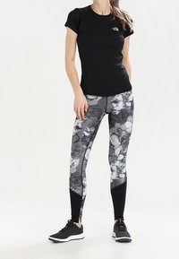 Svart tajt T-shirt med korta ärmar, grå mönstrade leggings med blommönster och svarta sportskor med vita sulor.