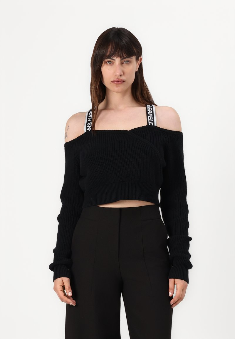 Schwarzer, gestrickter, schulterfreier, kurzer Pullover mit langen Ärmeln, der übergrobe Rippenstrickmuster und ein gewickeltes Design aufweist. Sichtbare schwarz-weiße Logokordeln.