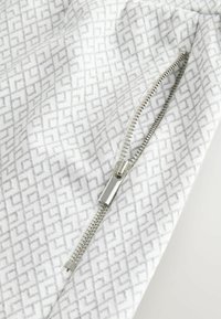 Witte stof met een lichtgrijs geometrisch patroon, met een zilveren ritsaccent aan de rechterkant. Zachte textuur, casual ontwerp.