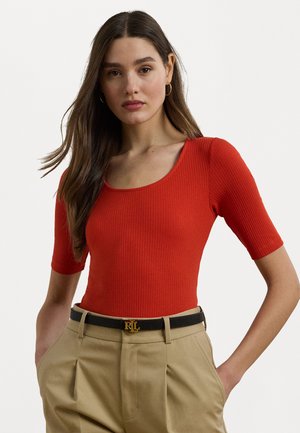Rød ribbet bodysuit med firkantet halslinje, korte ermer, kombinert med beltebukser i beige som har gullspenne detalj.