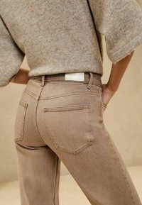 Beige džíny z denimu s těsným střihem, obsahující dvě zadní kapsy a jednoduchou etiketu na pase. Tkanina se zdá být měkká a mírně texturovaná.