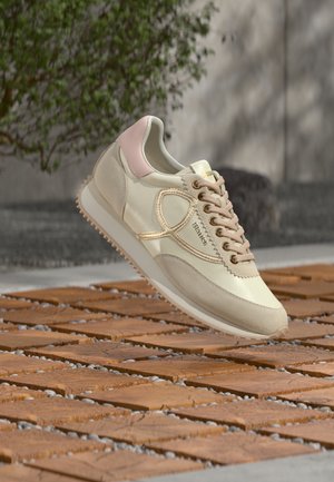 Beżowe sneakersy z górną częścią z gładkiej skóry, jasnoróżowymi akcentami na pięcie i teksturowaną podeszwą. Posiadają złote przeszycia i zaokrąglony kształt palców.