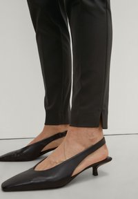 Slingerback schoenen van zwart leer met een puntige neus en een lage kittenhak; de broek is slim fit, op maat gemaakt, in het zwart, met een zijsplit aan de zoom.