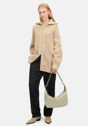 Beige gestrickte oversized Strickjacke mit hohem Kragen und Reißverschluss, kombiniert mit schwarzen Hosen und einer hellbeigen Umhängetasche. Braune Stiefeletten.