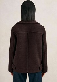 Hnědá fleecová bunda s uvolněným střihem, širokým límcem a knoflíkovými detaily na manžetách. Texturovaný povrch a jednobarevný design bez vzorů.
