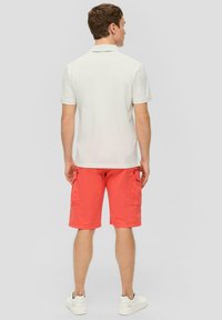 Männer's hellgraues Polohemd und korallenfarbene Cargo-Shorts mit Seitentaschen und lockerer Passform, kombiniert mit weißen Sneakers.