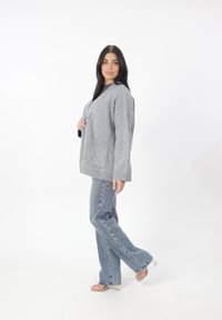 Cardigan grigio a maglia con scollo a V, tasche a toppa e orlo a costine, abbinato a jeans svasati blu chiaro e sandali trasparenti con tacco.