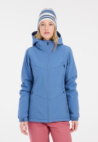 Blaue Softshell-Jacke mit Kapuze, ausgestattet mit Reißverschlusstaschen, einem strukturierten Design und verstellbaren Bündchen. Kombiniert mit einer gestreiften Strickmütze.