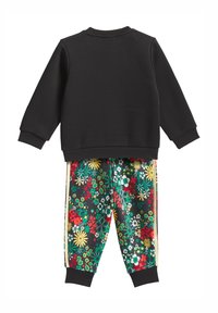 Juodas megztinis su ilgomis rankovėmis, derinamas su margais laisvalaikio kelnėmis, puoštomis žaliais, raudonais ir geltonais akcentais šonuose.