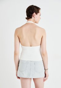 Bijela halter-top bluzica u paru s laganom suknjom svijetloplave i bijele prugaste boje, koja ima jednostavan dizajn bez vidljivih uzoraka ili akcenata.