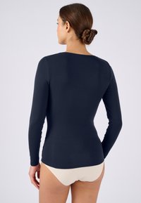 Langärmelige top in marineblauw, gemaakt van zachte stof, met een ronde halslijn en getailleerd ontwerp. Achteraanzicht toont gladde naden en minimale details.