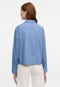 Light blue, collared, long-sleeve shirt with a relaxed fit and buttoned cuffs. Smooth fabric, slightly textured with vertical lines.