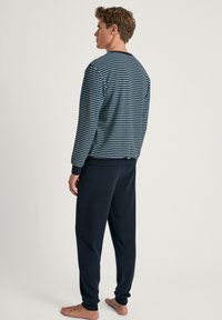 Marine gestreepte langwerpige top met geribde manchetten, gecombineerd met donkere joggingsbroek. Zacht materiaal, relaxte pasvorm, minimalistisch ontwerp, geen zichtbare patronen.