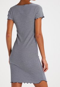 Pasiasta sukienka z krótkim rękawem w czarno-białe wzory, o dopasowanym kroju, okrągłym dekolcie i falbaniastym wykończeniu dołu. Gładka faktura materiału.