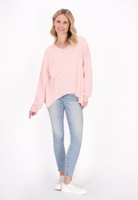 Pullover oversize in maglia a nido d'ape rosa con scollo a V e spalle ribassate, abbinato a jeans skinny in lavaggio chiaro e sneaker bianche.