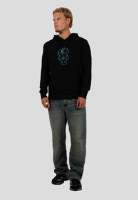 Czarna bluza z kapturem z kolorowym graficznym wzorem z przodu, w połączeniu z jasnoniebieskimi dżinsami i czarnymi trampkami. Casualowy krój i wygodny styl.