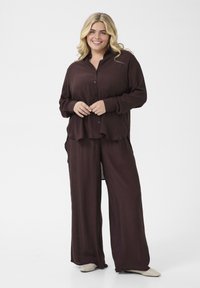 Bordó blůza a široké kalhoty, vyrobené z měkké tkaniny. Blůza má knoflíky a volný střih; kalhoty mají elegantní drapérii.